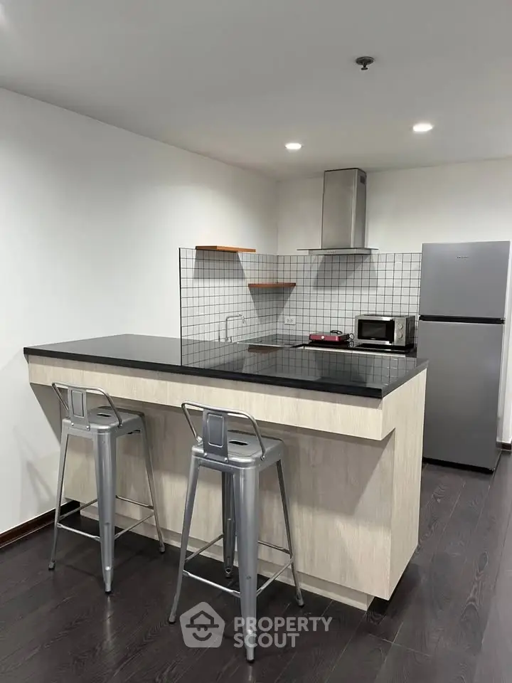 Modern kitchen with sleek island, stainless steel appliances, and stylish bar stools in a contemporary apartment.