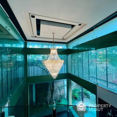 Luxurious modern interior with stunning chandelier and glass walls overlooking lush greenery.