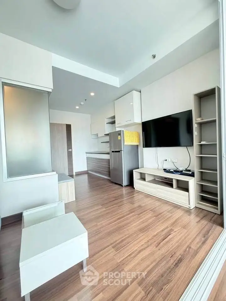Modern living room with sleek wooden flooring and stylish kitchen area in open layout apartment.
