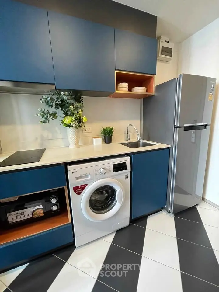 Modern kitchen with blue cabinets, washing machine, and stainless steel fridge