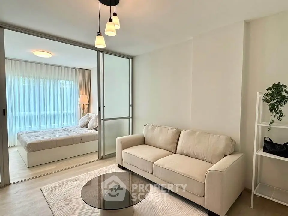 Modern living room with cozy sofa and elegant bedroom view through glass doors.