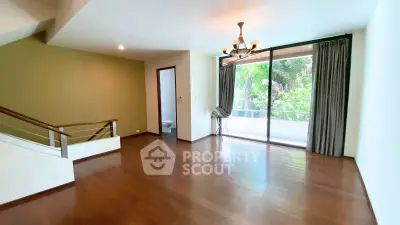 Spacious living room with wooden floors and large window overlooking greenery.