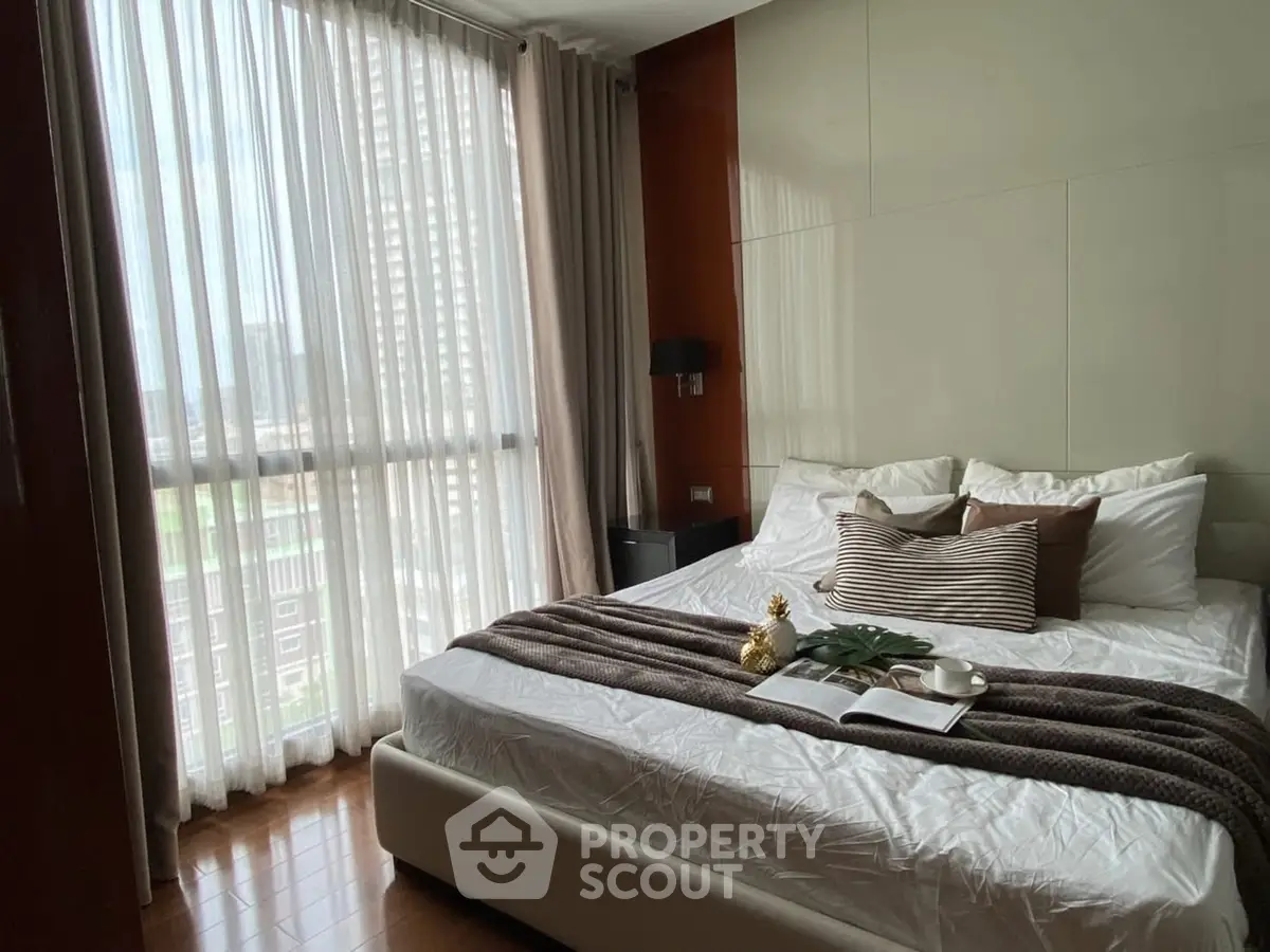 Cozy bedroom with large windows and modern decor in a high-rise apartment.