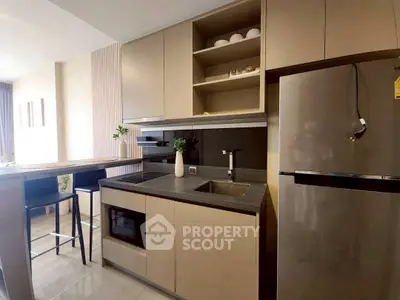 Modern kitchen with sleek cabinets, stainless steel fridge, and breakfast bar in stylish apartment.