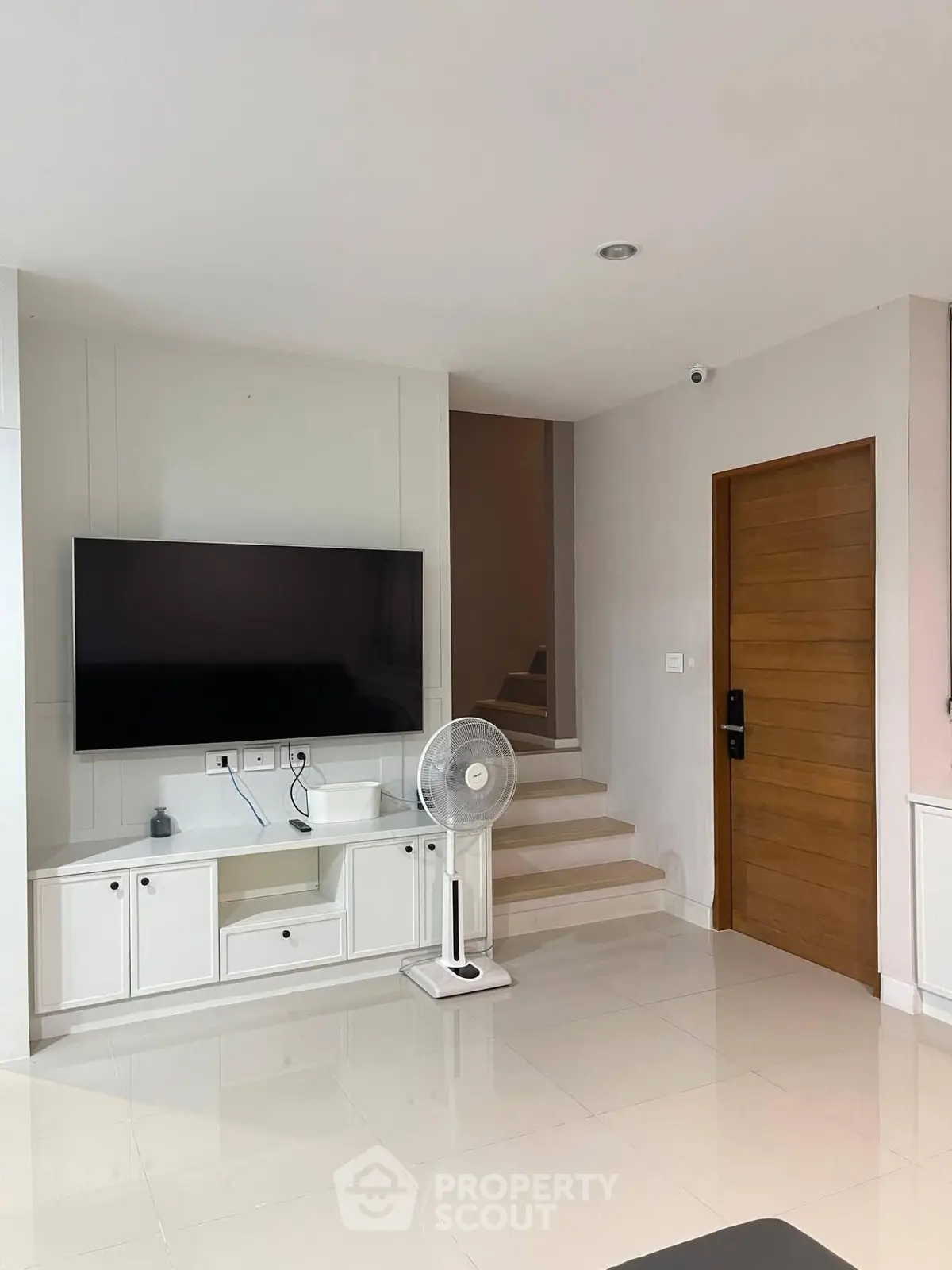 Modern living room with sleek TV setup and wooden door, featuring minimalist design and neutral tones.