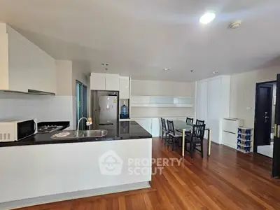 Spacious modern kitchen with sleek design and dining area, featuring wooden flooring and ample storage.