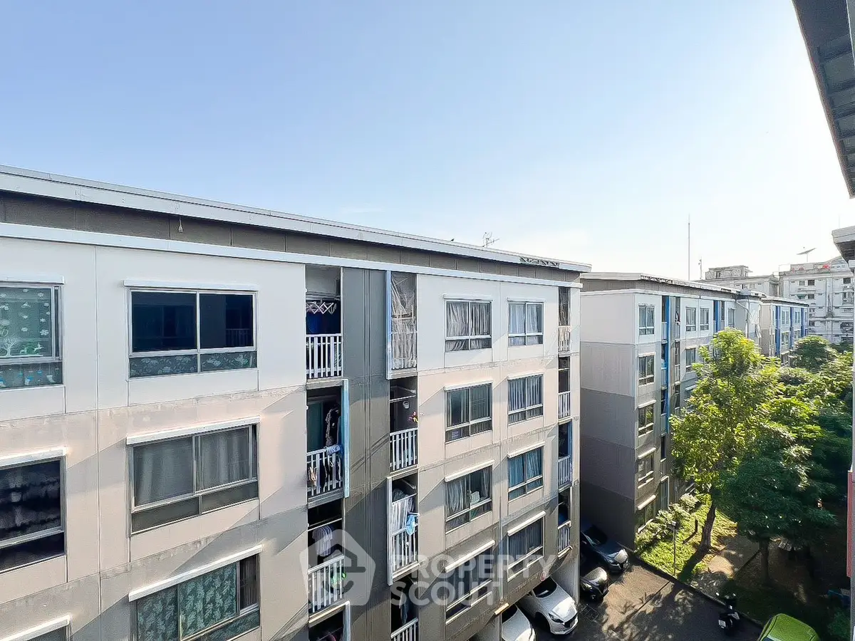Modern apartment building exterior with lush greenery and clear blue sky.