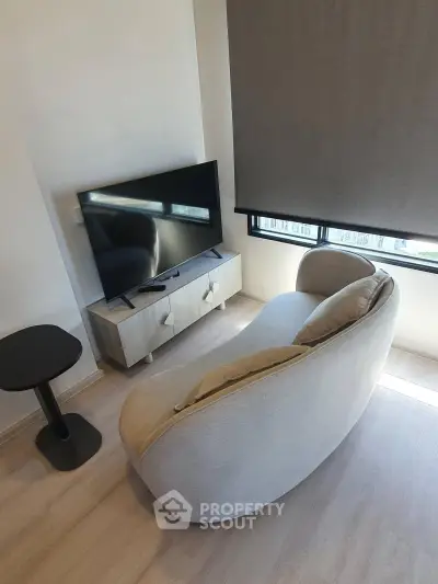Modern living room with stylish sofa and flat-screen TV, featuring natural light and minimalist decor.