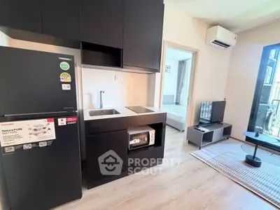 Modern compact kitchen with sleek black cabinets and appliances in a cozy apartment setting.