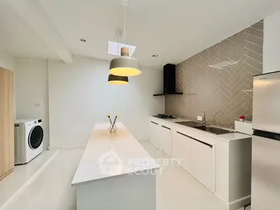 Modern kitchen with sleek design, featuring an island, gas stove, and washing machine.
