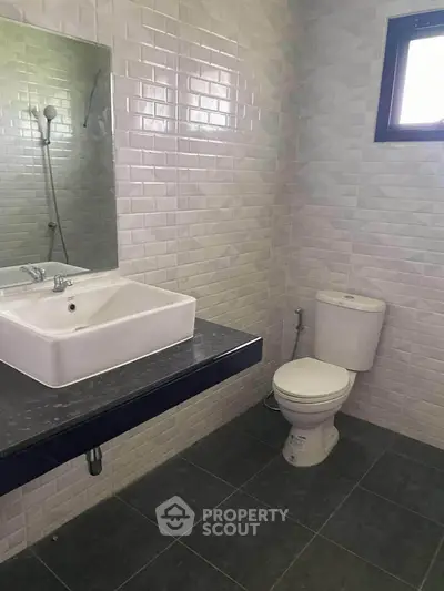 Modern bathroom with sleek sink and toilet, featuring stylish tiled walls and flooring.