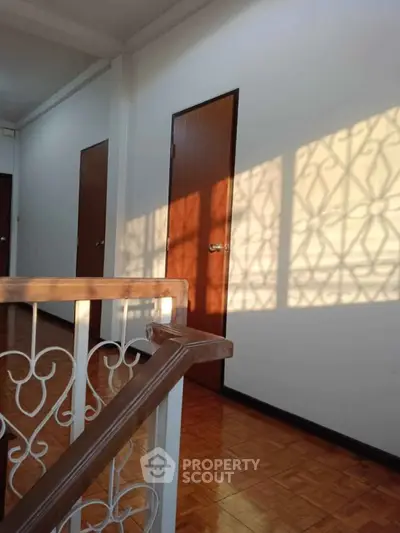 Charming hallway with wooden doors and elegant railing, bathed in warm sunlight.