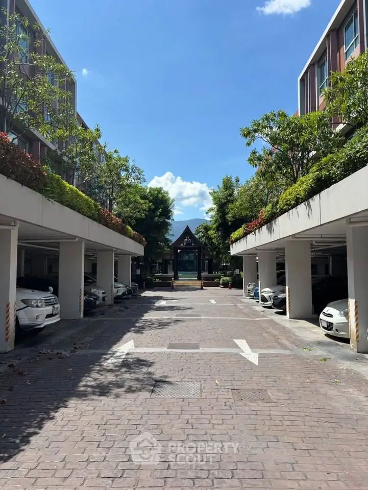 Charming residential complex with lush greenery and ample parking space under a clear blue sky.