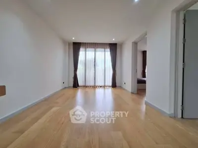 Spacious empty living room with wooden flooring and large window with curtains.
