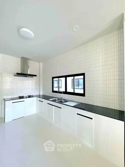 Modern kitchen with sleek white cabinets and black countertops, featuring a gas stove and large window.