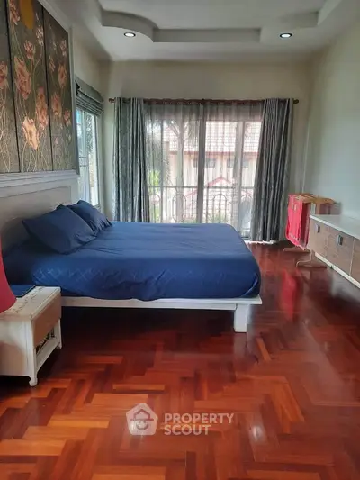 Spacious bedroom with elegant wooden flooring and large windows offering natural light.