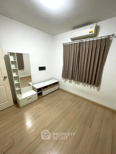 Spacious bedroom with modern flooring and air conditioning, featuring a stylish mirror and storage unit.