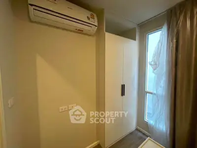 Compact bedroom with air conditioning and wardrobe, featuring a window with sheer curtains for natural light.