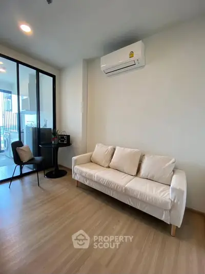 Modern living room with white sofa and air conditioning, featuring sleek glass doors leading to a balcony.