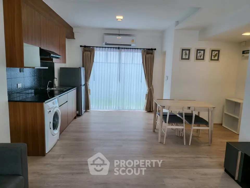 Modern open-plan living room with kitchen and dining area, featuring wooden flooring and natural light.