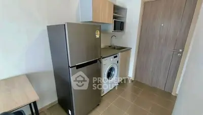 Compact kitchen with fridge, washing machine, and microwave in modern apartment.