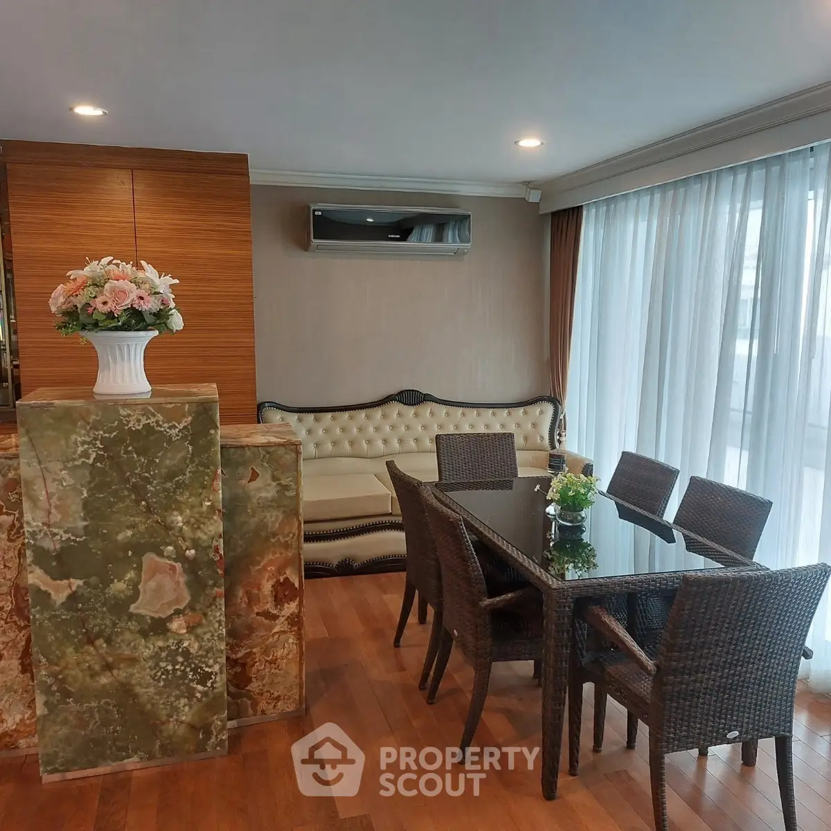 Elegant dining area with wicker chairs and glass table, featuring a plush sofa and floral centerpiece.