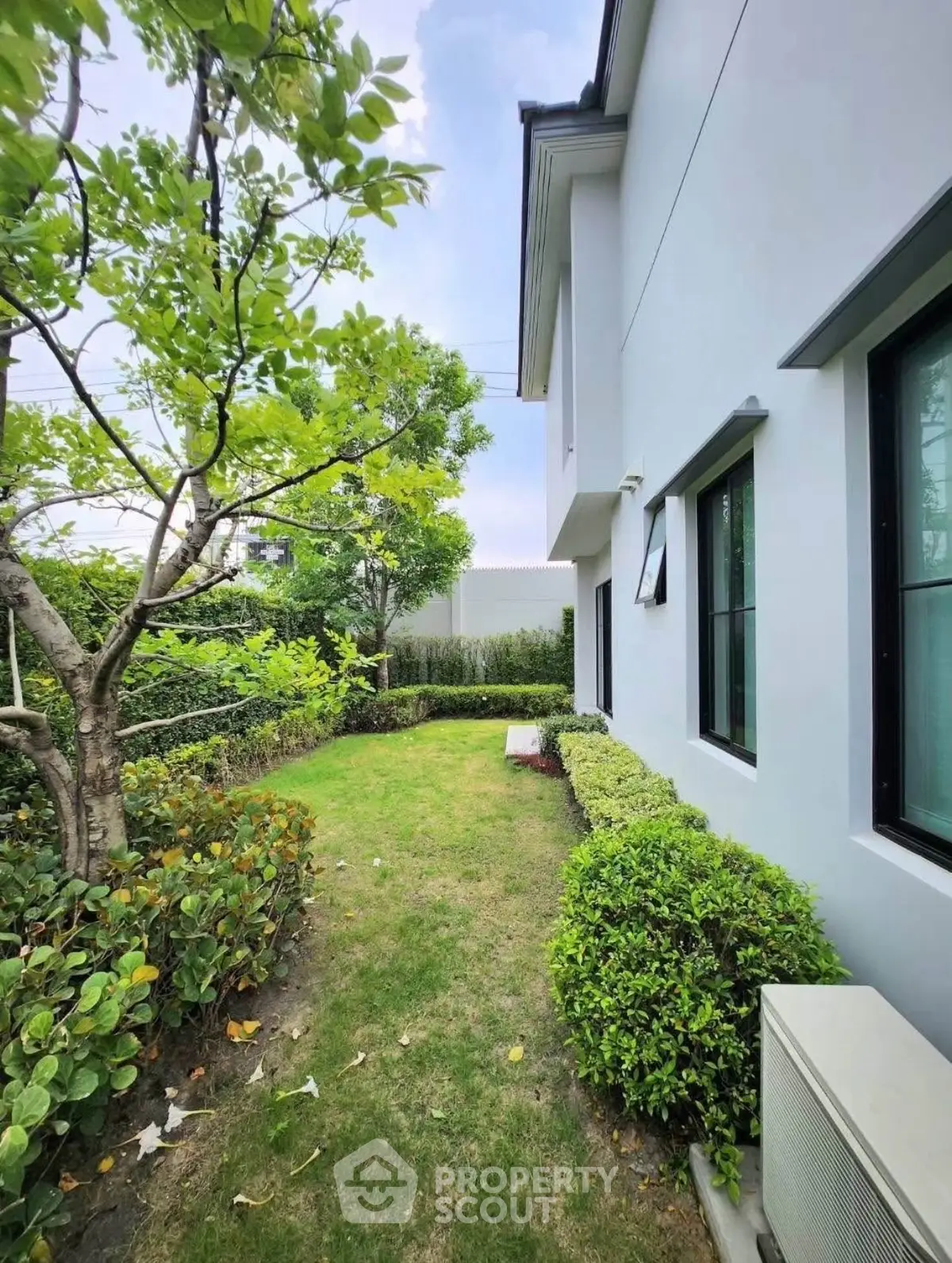 Charming garden view beside modern house with lush greenery and manicured hedges.