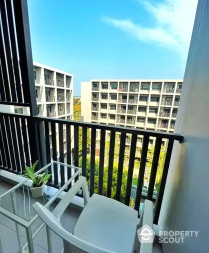 Inviting balcony with modern white chairs overlooking a serene garden and neighboring buildings, perfect for relaxing outdoor moments.