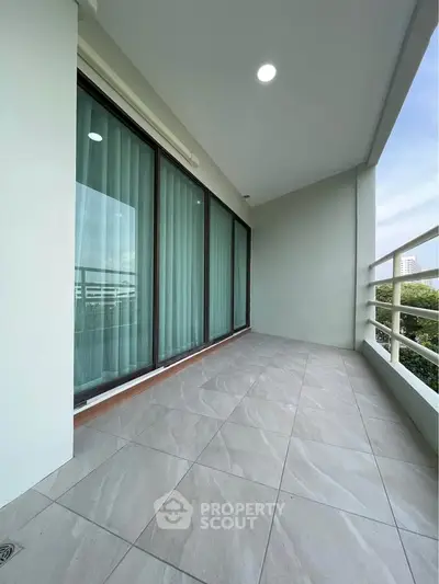 Spacious balcony with modern tiles and glass doors, perfect for relaxation.