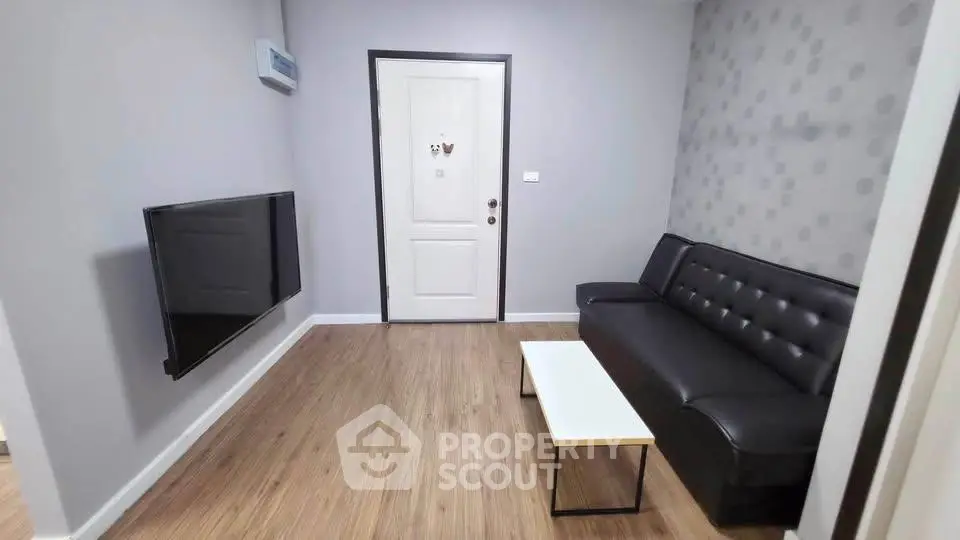 Modern living room with sleek black sofa and wall-mounted TV, featuring stylish wooden flooring.
