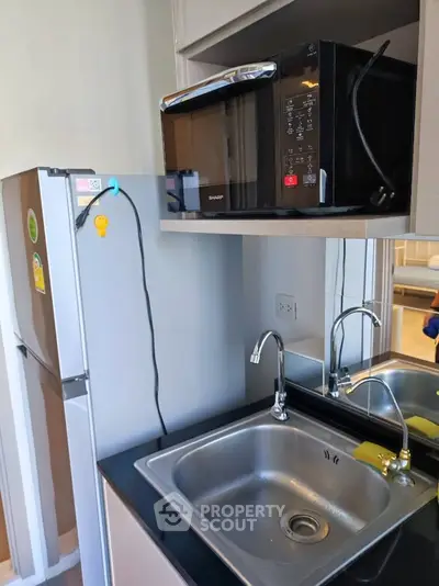 Compact kitchen with modern appliances including microwave and fridge, featuring a sleek stainless steel sink.