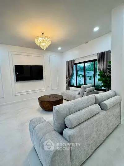 Elegant living room with modern gray sofas, large TV, and stylish chandelier, perfect for relaxation.