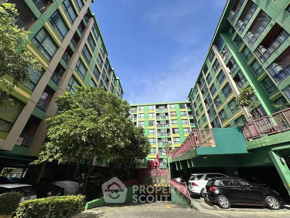 Vibrant multi-story residential building with parking area and lush greenery.