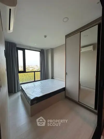 Modern bedroom with large window and mirrored wardrobe in a high-rise apartment.