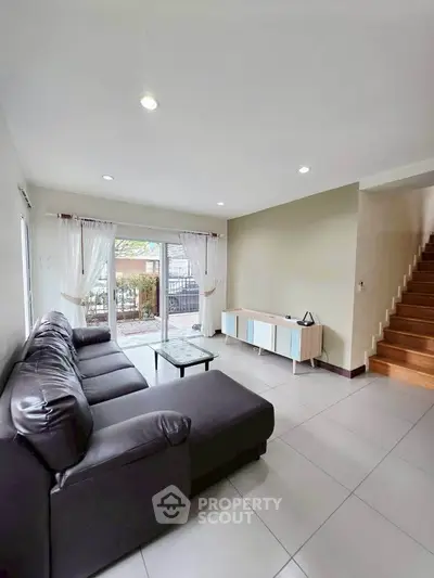 Spacious living room with modern sofa and natural light, leading to a cozy outdoor area.