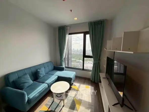 Modern living room with city view, featuring a stylish blue sofa and large window.