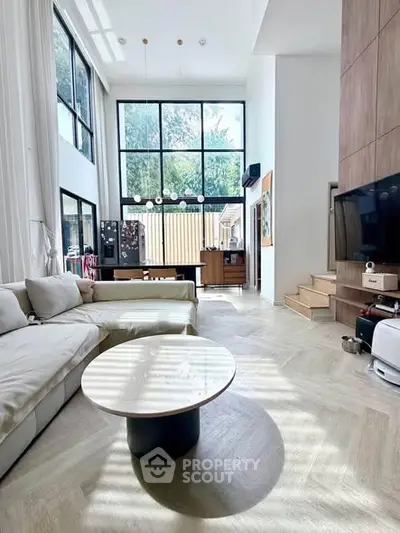 Spacious modern living room with high ceilings and large windows, featuring elegant furniture and natural light.