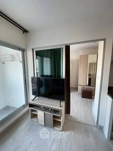 Modern apartment interior with TV and sliding glass doors leading to a bedroom.