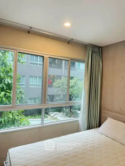 Cozy bedroom with large windows offering a serene garden view in a modern apartment.