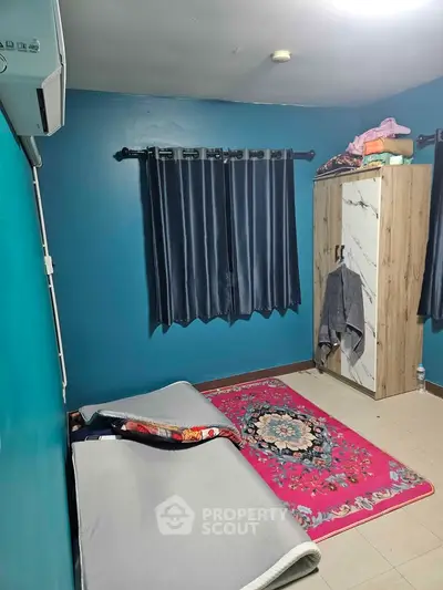 Cozy bedroom with vibrant blue walls, minimalist decor, and natural light from window.
