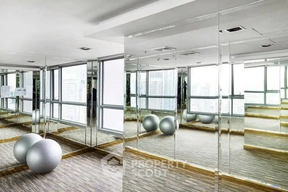 Luxurious gym with mirrored walls and city view in modern high-rise building.