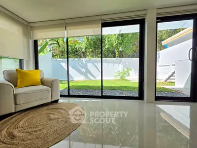 Bright living room with large glass doors opening to a lush garden, featuring a cozy armchair and stylish decor.
