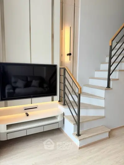 Modern living room with sleek staircase and mounted TV, featuring minimalist design and elegant lighting.