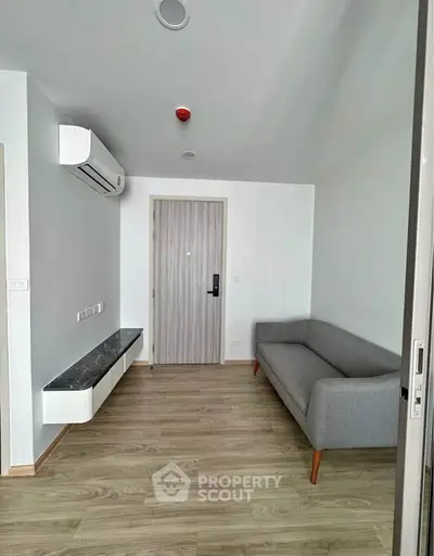 Modern living room with sleek gray sofa and wall-mounted air conditioner in minimalist apartment.