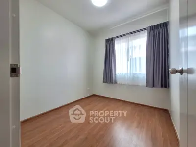 Spacious and well-lit bedroom with polished wooden flooring and large window draped with elegant dark curtains.
