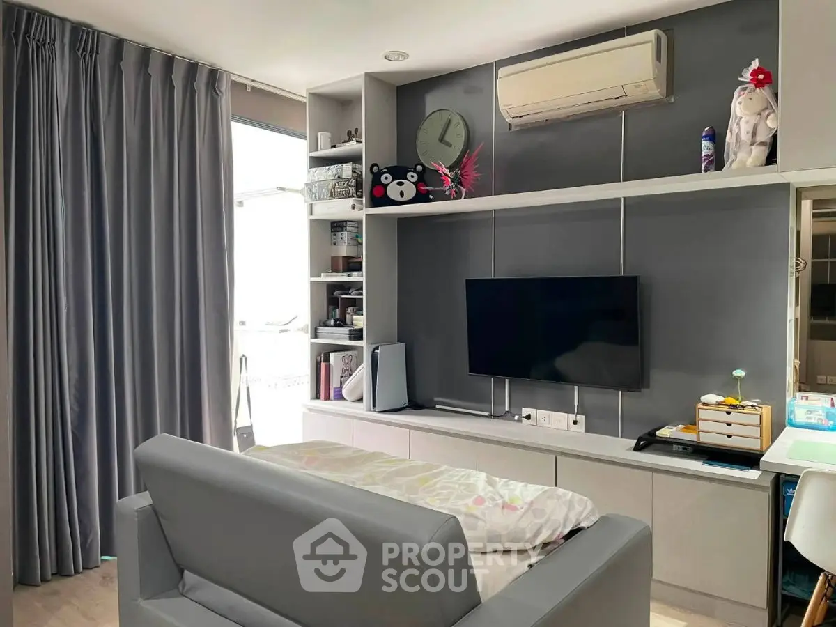 Modern living room with sleek gray sofa, wall-mounted TV, and stylish shelving unit.