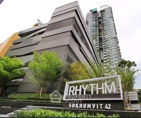 Modern high-rise building with sleek design at Rhythm Sukhumvit 42, surrounded by lush greenery.