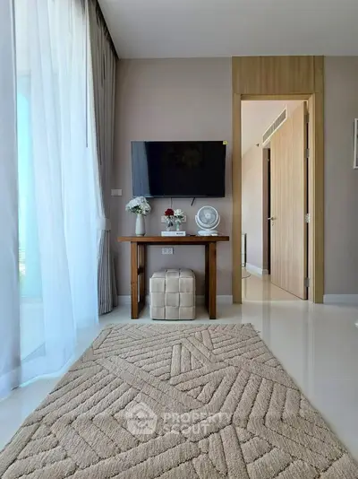 Modern living room with elegant decor and wall-mounted TV, featuring a plush rug and natural light.
