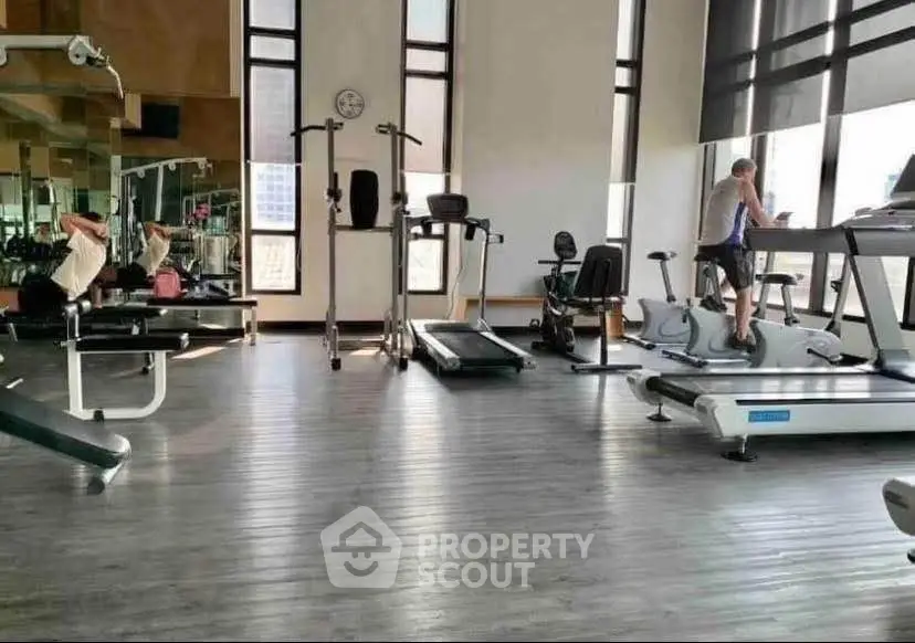 Spacious gym with modern fitness equipment and large windows for natural light.