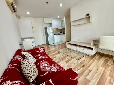 Modern living room with red sofa and open kitchen layout, featuring sleek wooden flooring.